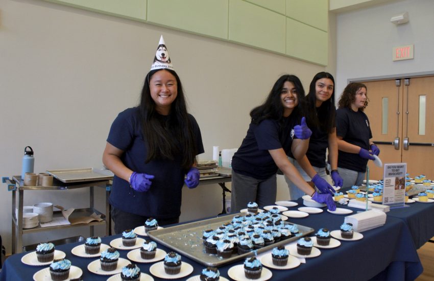 A student smiling while handing out cupcakes at an event for Jonathan's birthday